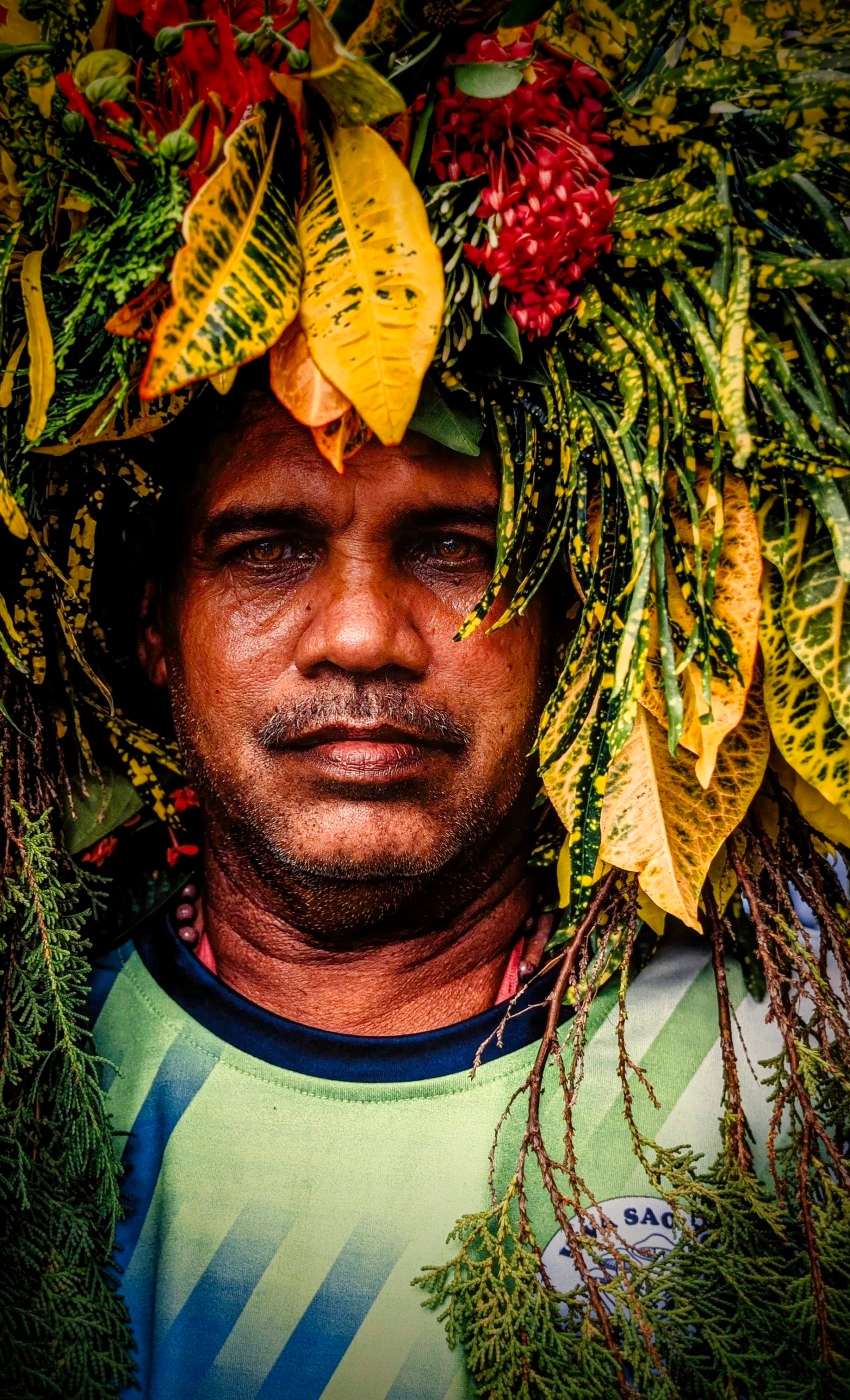 Colorful portrait of a man wearing a vibrant headpiece made of leaves and flowers.