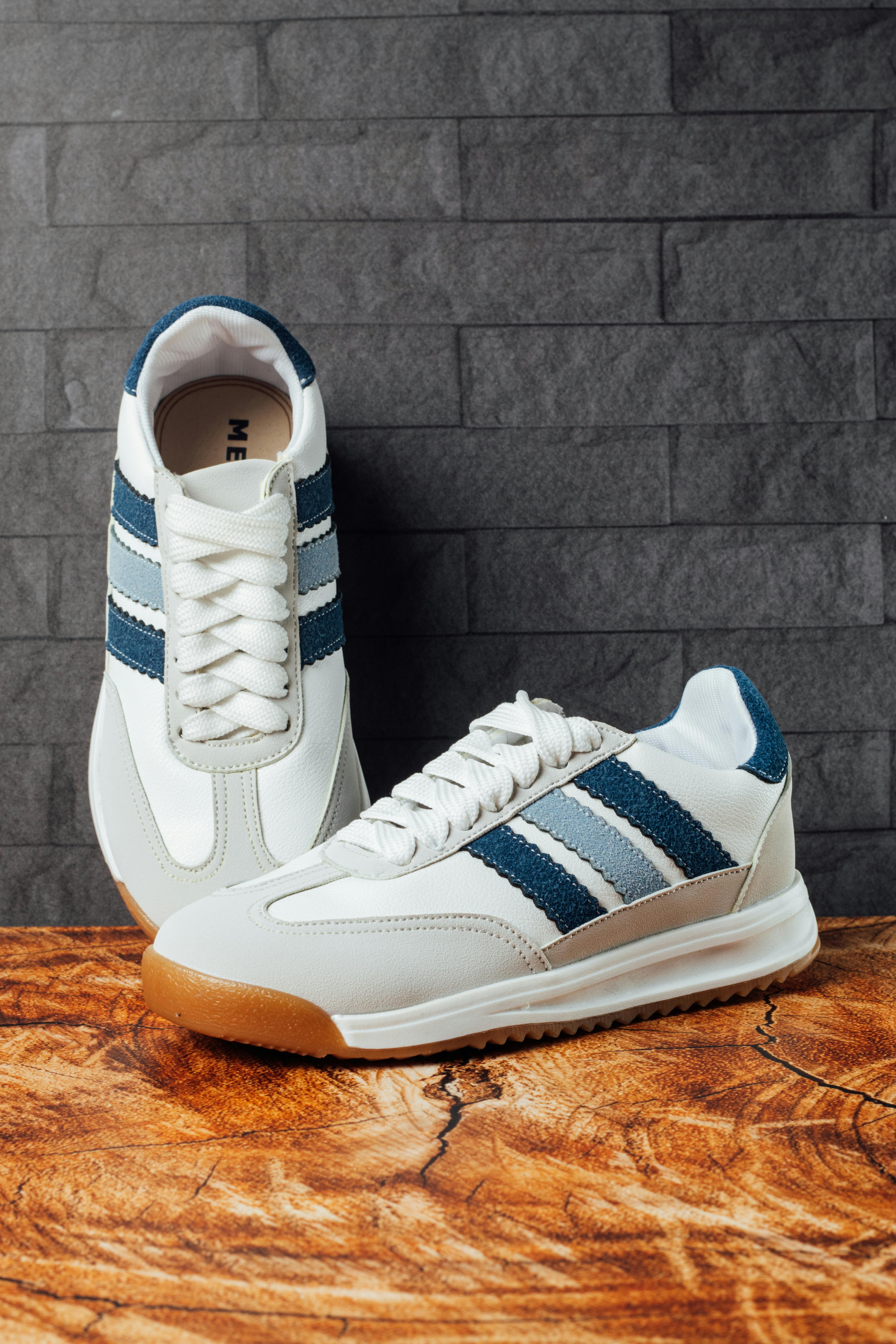 A pair of modern white and blue sneakers showcased on a wooden surface, perfect for casual and sporty fashion.