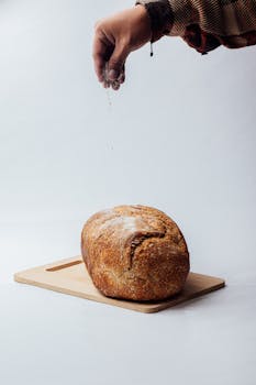 Freshly baked artisan loaf being salted on a wooden board.