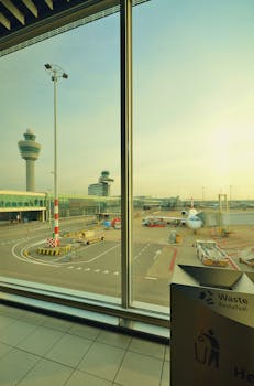 Photo by ClickerHappy Perspective of airport runway and airplane seen from terminal window during day.
