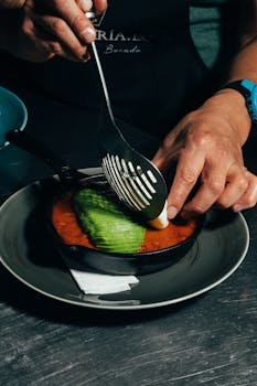 Close-up of chef assembling a gourmet dish with avocado in a skillet.