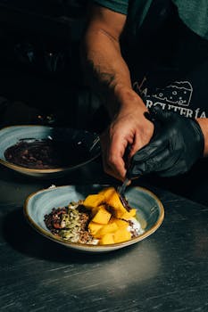 A chef skillfully garnishes a vibrant mango dish, adding a touch of elegance in a professional kitchen setting.