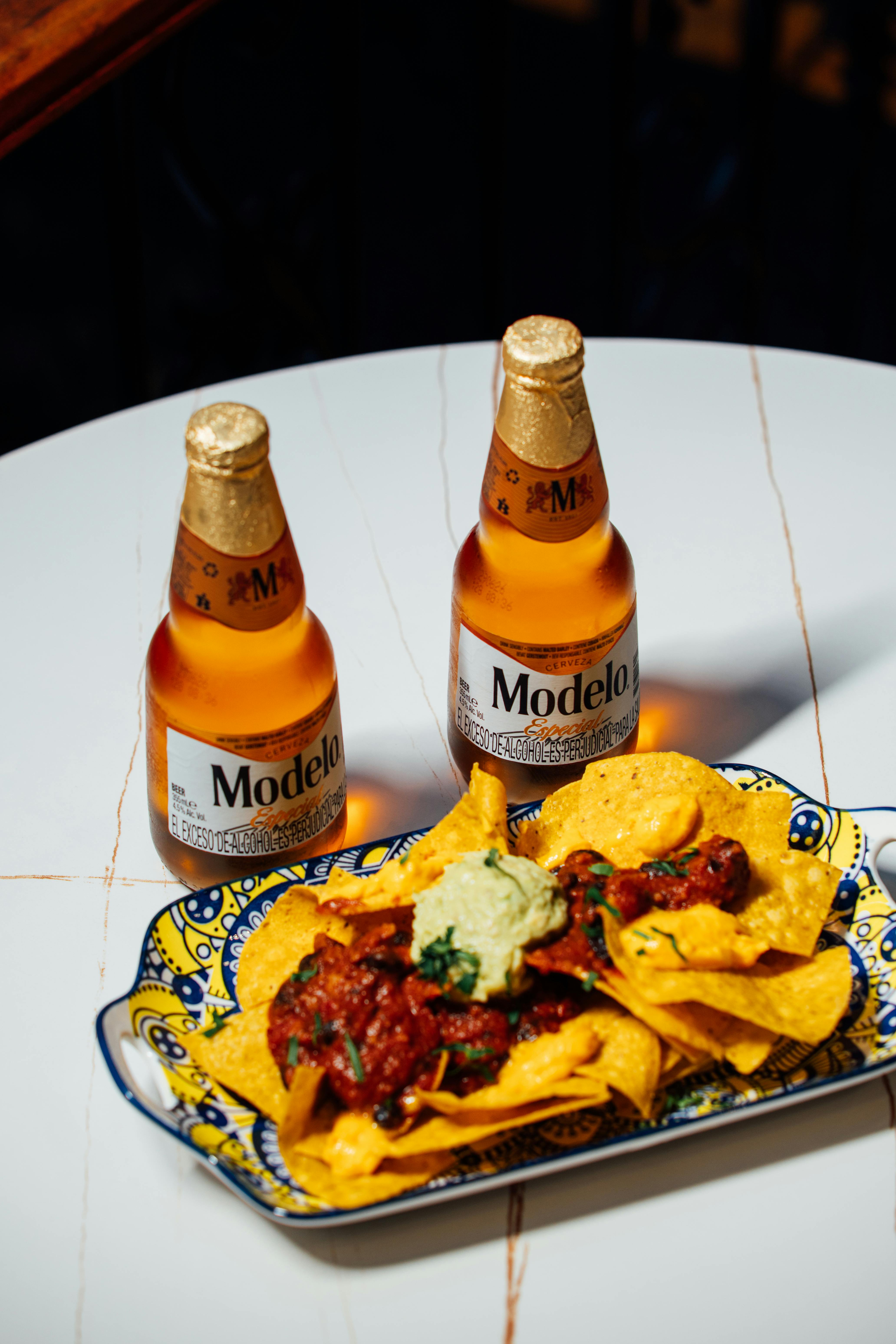 Gratis Deliziosa birra messicana con nachos ricoperti di salsa e guacamole su un piatto vivace. Foto a disposizione