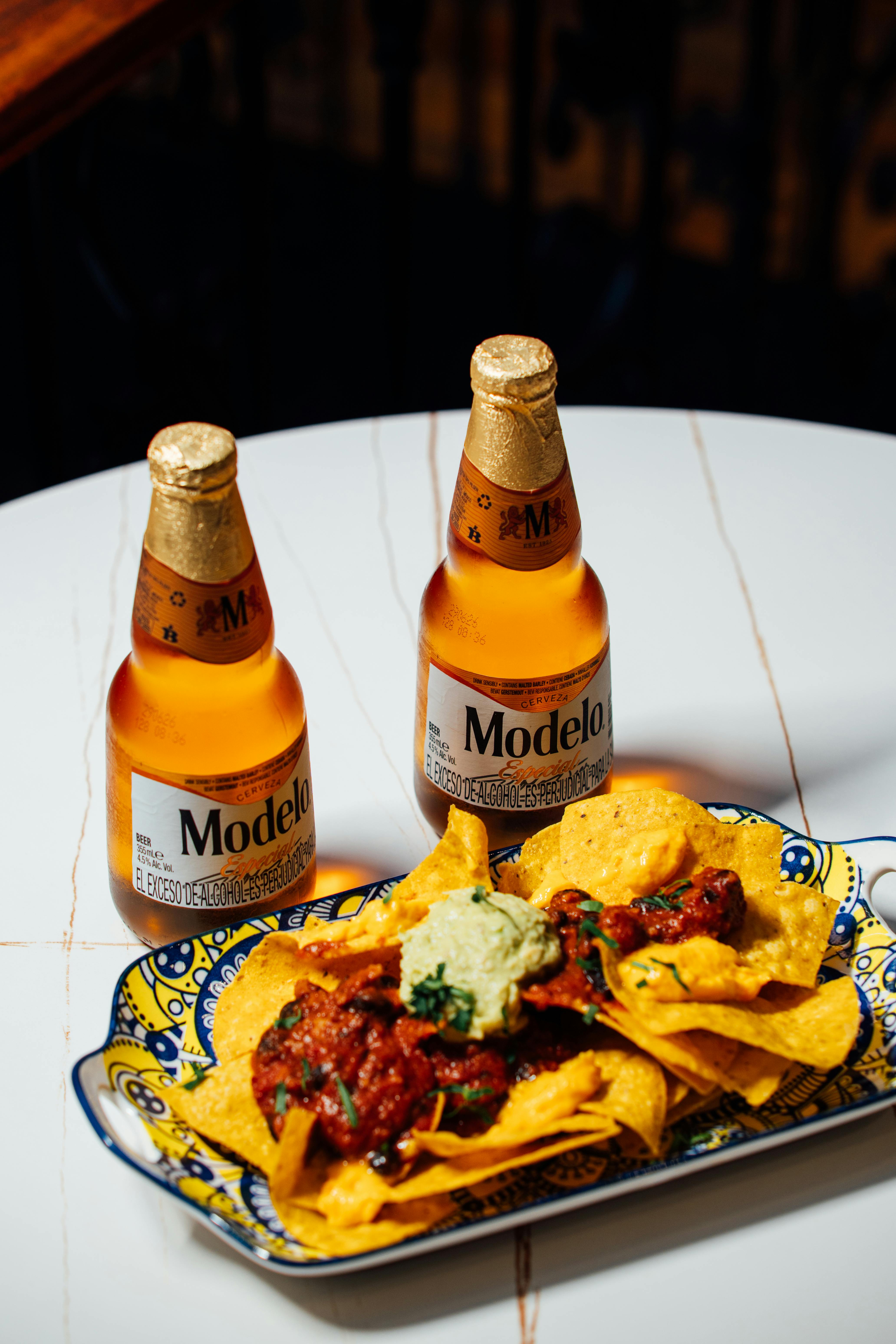 ingyenes Hűtött Modelo sörösüvegek egy tányér nachossal és salsával, stílusos terítéken. Stockfotó