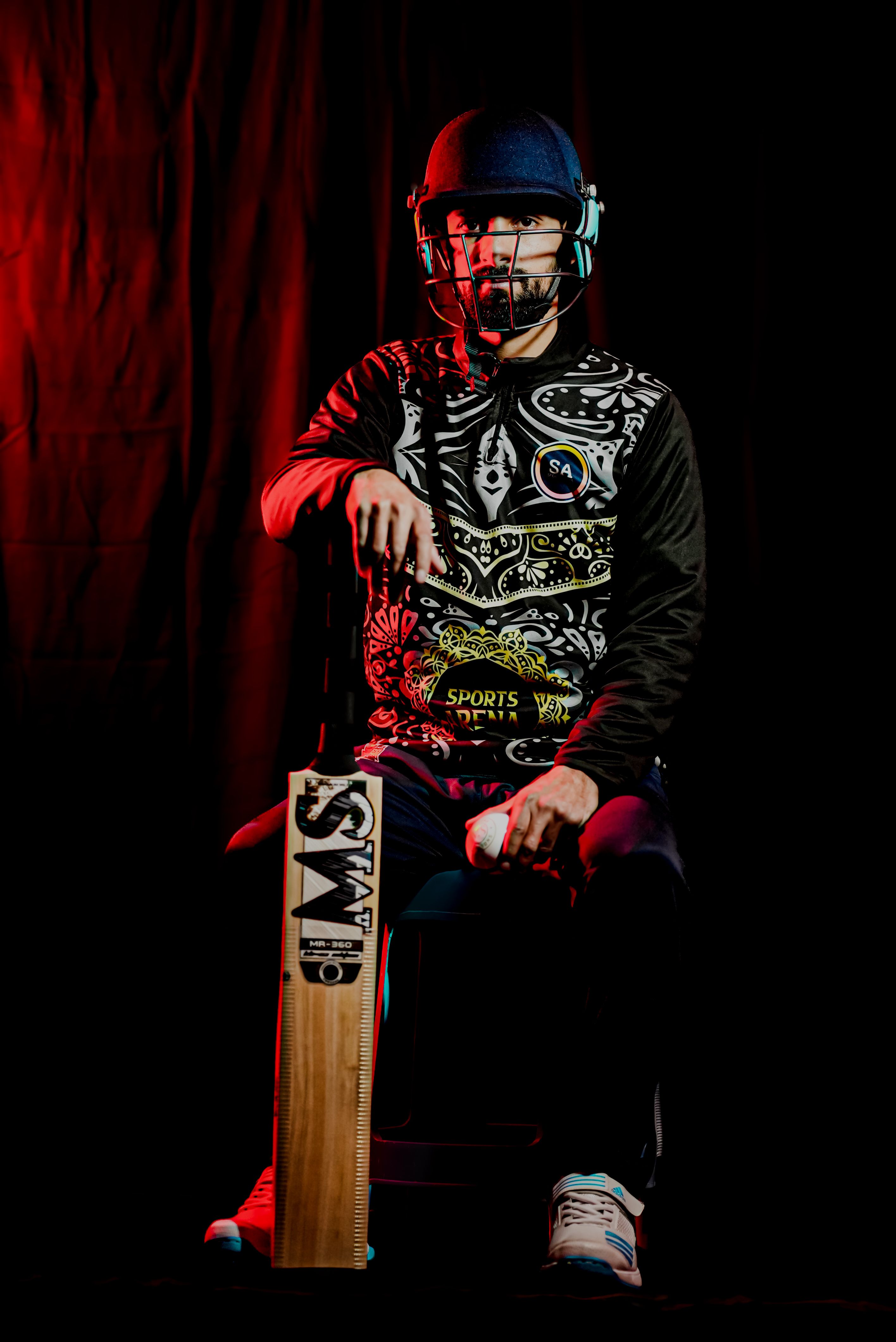 A cricket player in full gear poses with a bat against a dramatic backdrop.