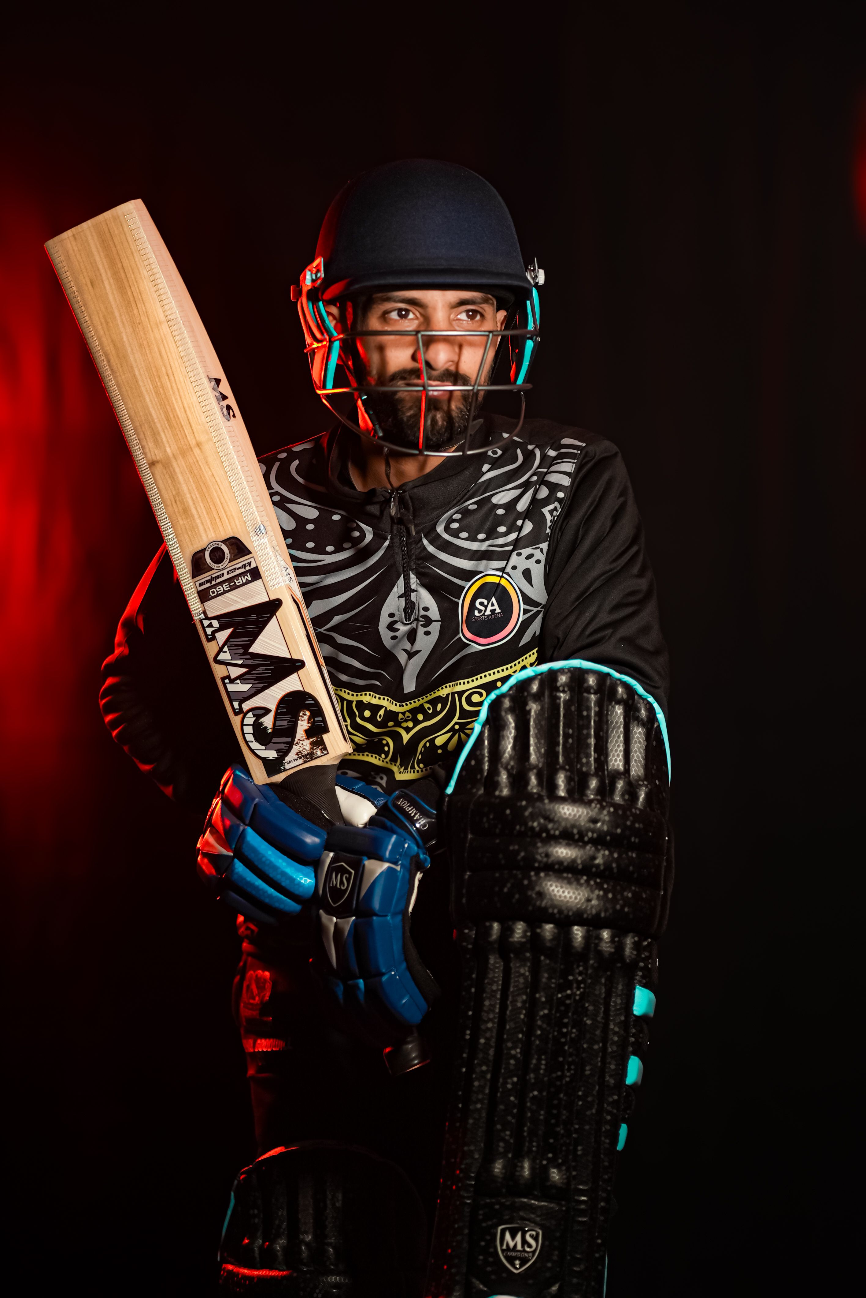 Experienced cricket player wearing full gear, holding a bat, in a dramatic studio setting.