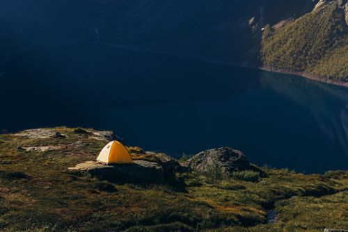Free A solitary yellow tent on a grassy hill overlooking a tranquil mountain lake at dawn. Stock Photo