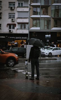 A lone figure with an umbrella stands on a rainy Madrid street, capturing urban life.