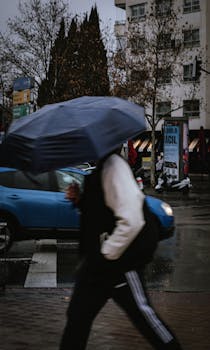 Blurred pedestrian with umbrella crossing a rainy city street.