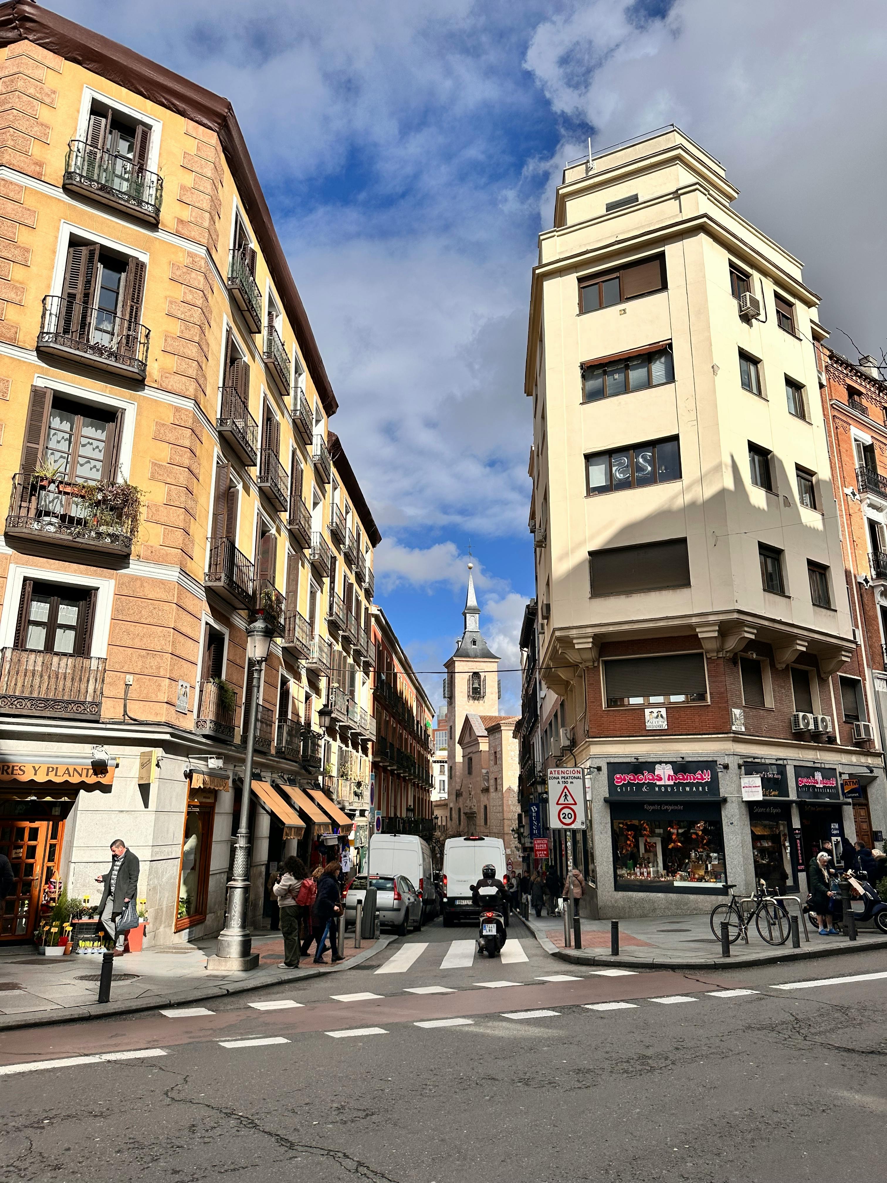 Vibrant street scene in Madrid featuring classic architecture and a church in the background under a blue sky.