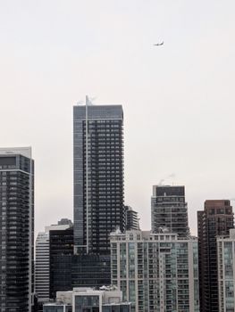 Overcast view of Toronto's skyscrapers with an airplane in the sky, capturing urban architecture.