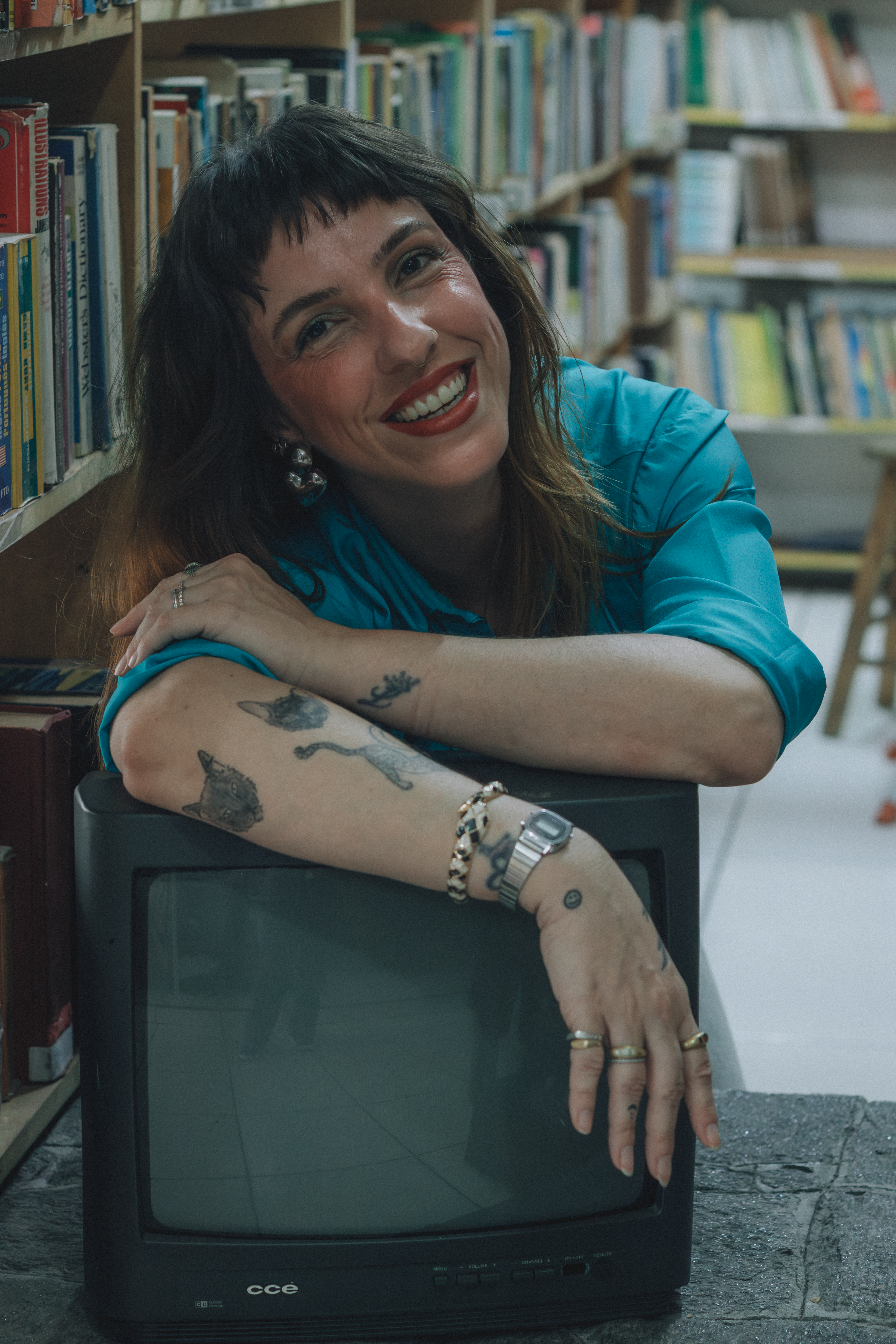 Woman with tattoos and vintage TV smiling in a cozy library setting.