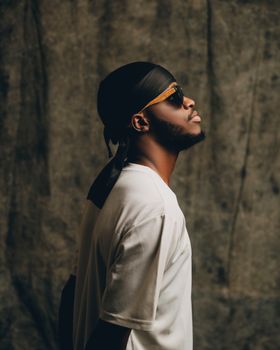 Side profile of a stylish man wearing sunglasses and a bandana against a textured background.