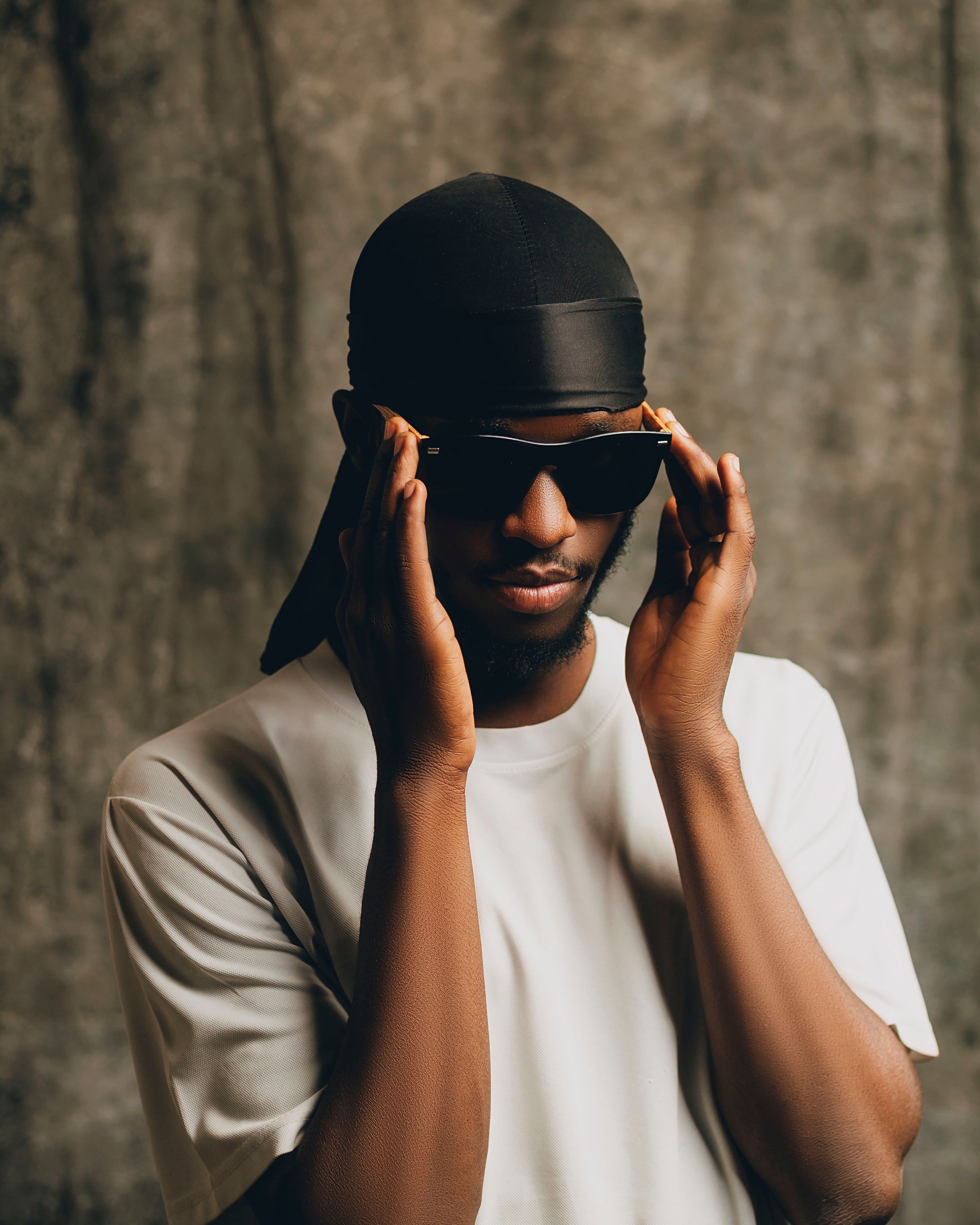 Stylish adult wearing sunglasses and a durag against a textured backdrop.