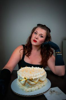 Elegant woman with red lipstick sitting by a decorative cake. Glamorous and classy setting.