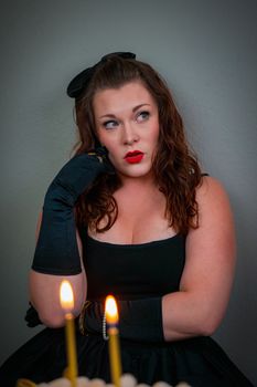 Portrait of a woman in a black dress posing thoughtfully near lit candles.