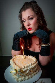 Woman in evening wear pondering over a single candle birthday cake.