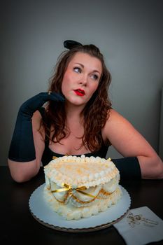 Stylish woman in evening gloves posing with an ornate cake in an indoor setting.
