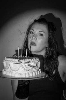 A black and white image of a woman holding a decorated birthday cake.
