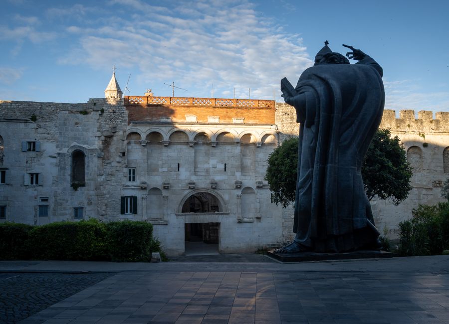 View of the historic Gregory of Nin statue in front of Split's medieval city walls, a notable cultural landmark.