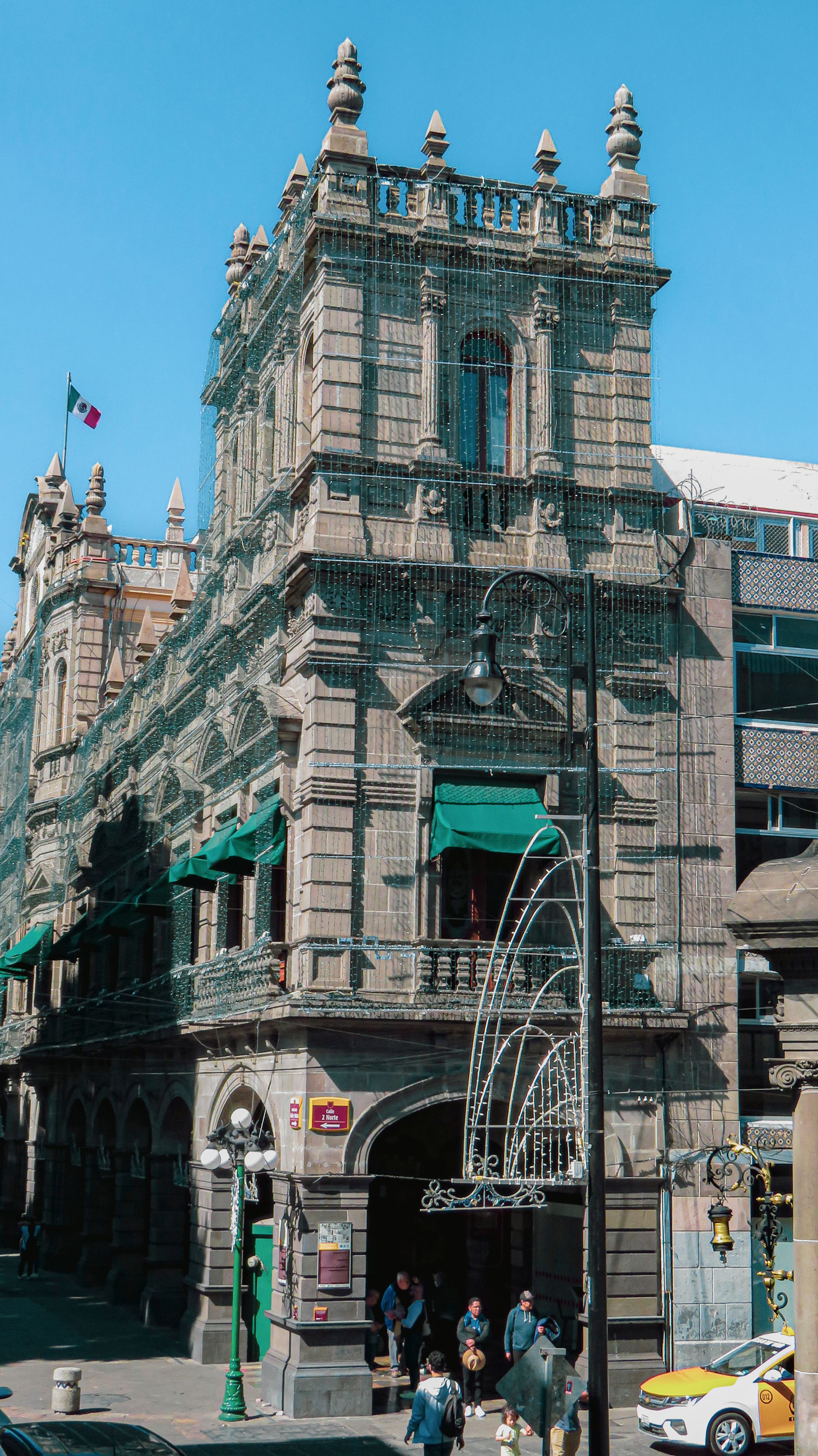 Ornate historic building in Puebla, Mexico, showcasing colonial architecture with people and taxi nearby.