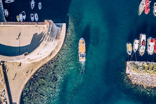 Drone shot of Dubrovnik harbor showcasing clear turquoise waters and moored boats from above.