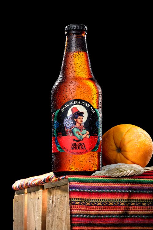 Free Bottle of Huaracina Pale Ale Sierra Andina with vibrant traditional fabric and orange. Stock Photo