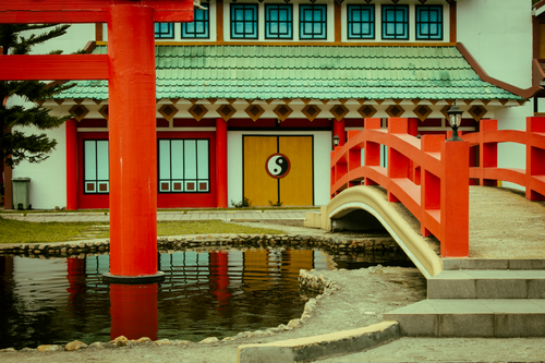 Free Serene Japanese garden featuring a vibrant red bridge, torii gate, and yin yang symbol. Stock Photo