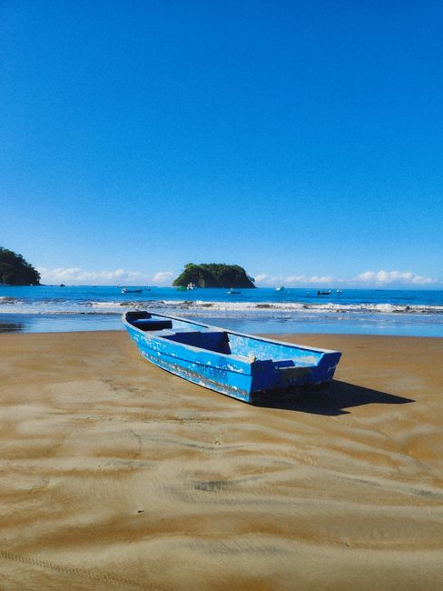 A solitary blue boat rests on the sandy shores of Sámara Beach, Costa Rica, under a clear blue sky.