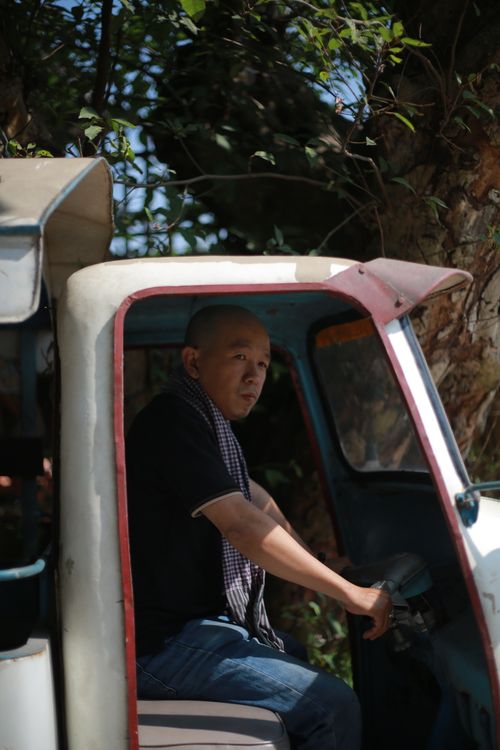Free A man drives a tuk-tuk in a leafy outdoor setting, capturing a moment of daily life. Stock Photo