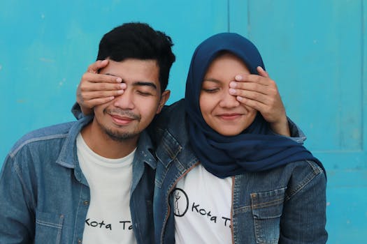 一对快乐的亚洲年轻夫妇穿着牛仔夹克，顽皮地用手遮住了彼此的眼睛