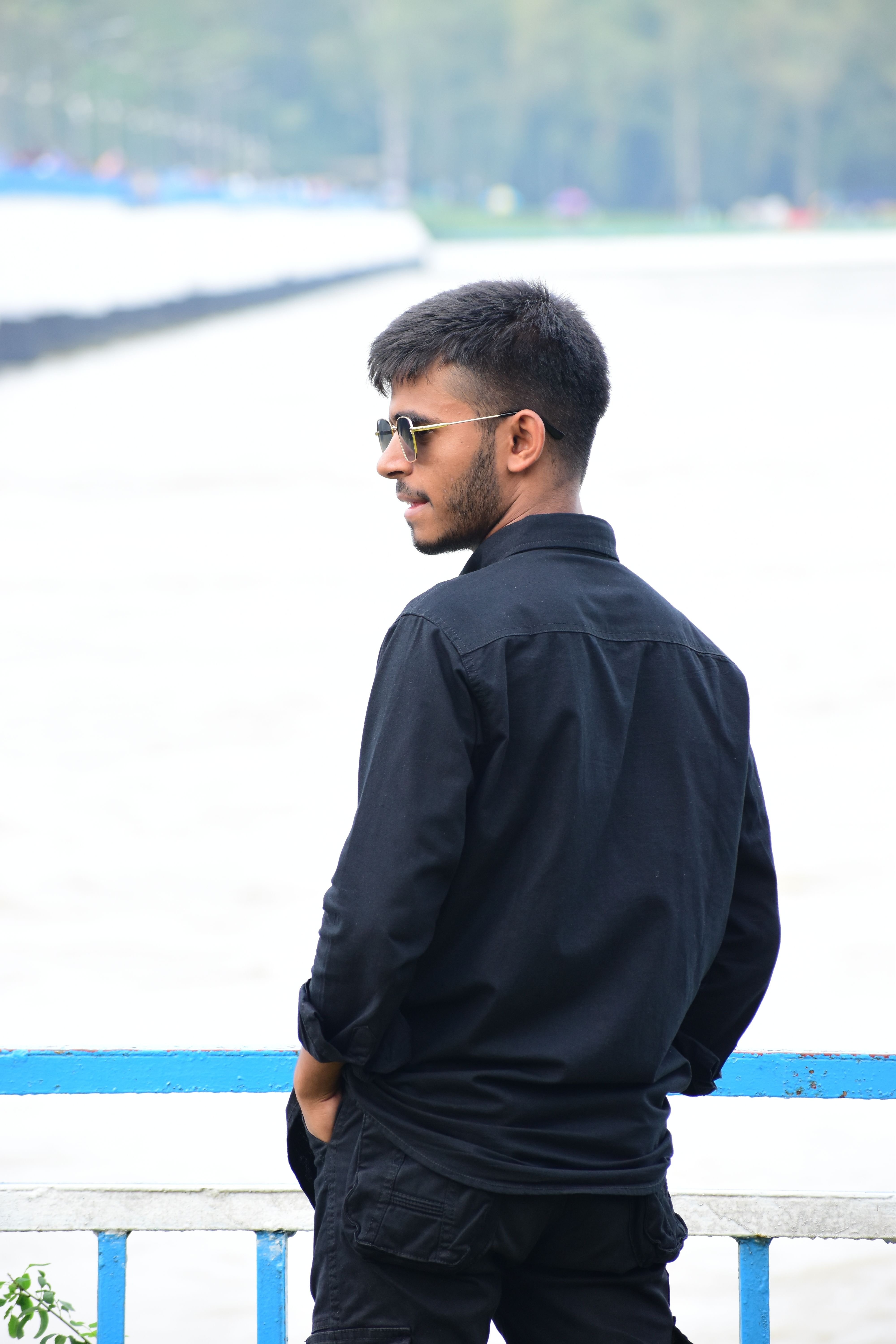 A young man in sunglasses stands by a waterfront in Dhaka, Bangladesh.