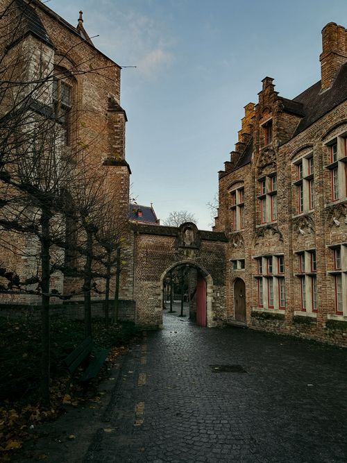 Free A picturesque stone alleyway in Bruges, Belgium, showcasing medieval architecture during a serene fall evening. Stock Photo