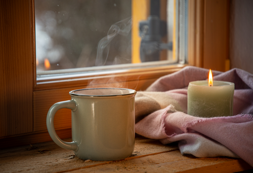 Free A warm cup of coffee and a candle create a cozy ambiance by the window. Stock Photo