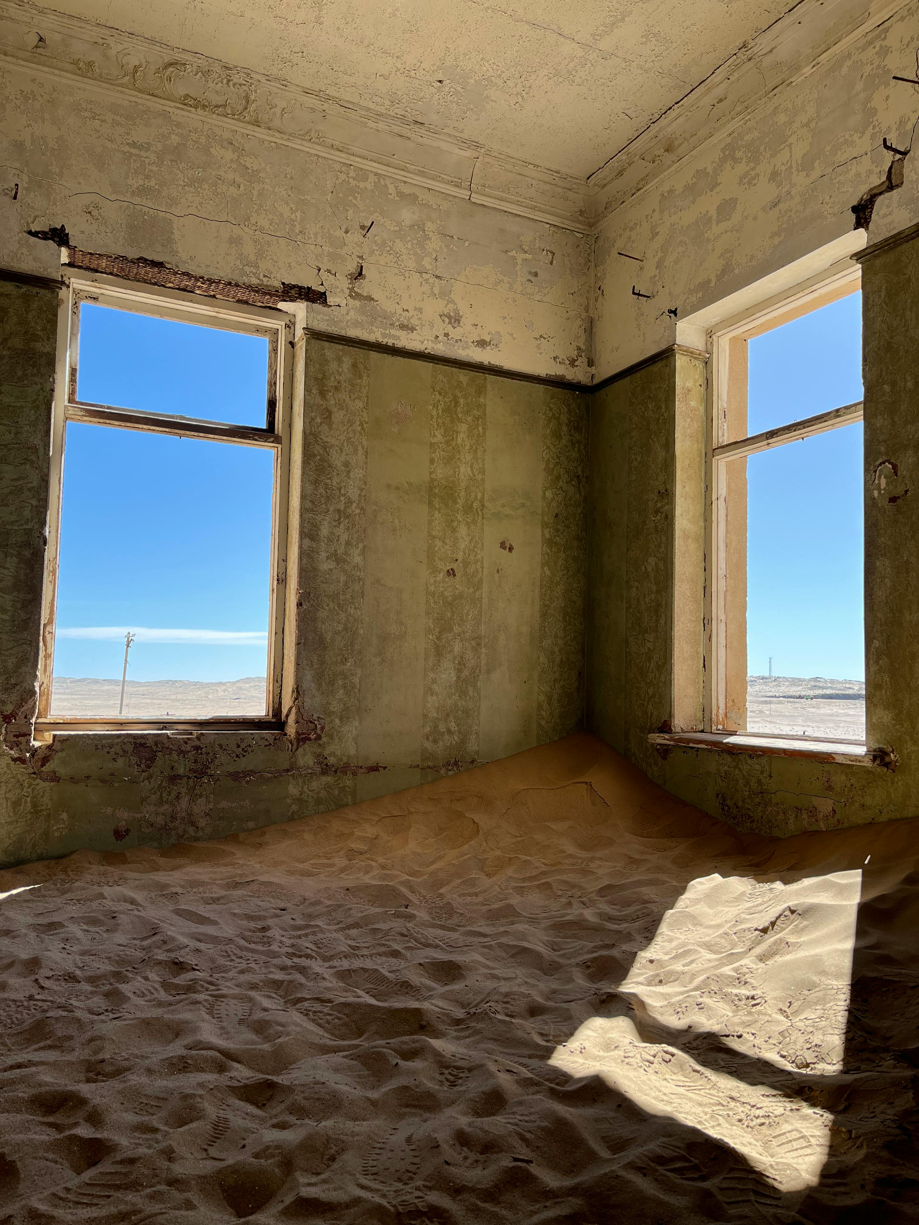 Sunlit deserted room filled with sand dunes, creating an eerie contrast of nature indoors.