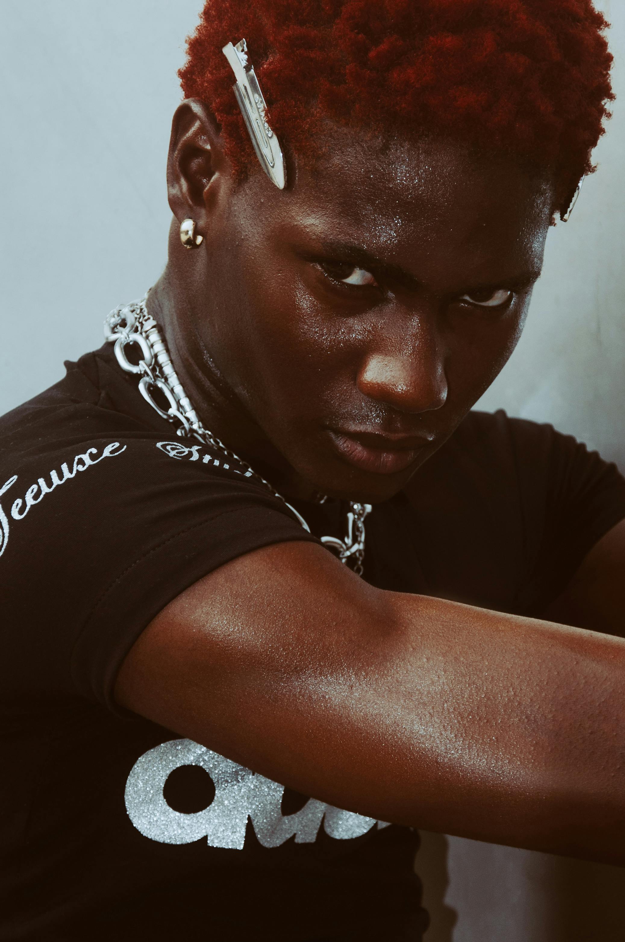 Close-up portrait of a young man in a black shirt with vibrant hair, exuding confidence.