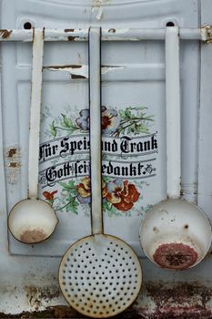 Rustic vintage kitchen utensils hanging against an ornate floral background.