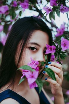 A woman with dark hair poses gracefully amidst vibrant pink bougainvillea blossoms in a garden setting.