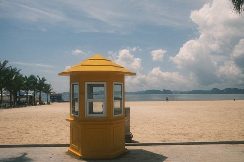 Free A vibrant yellow booth stands on a serene beach with clear blue skies and distant islands. Stock Photo