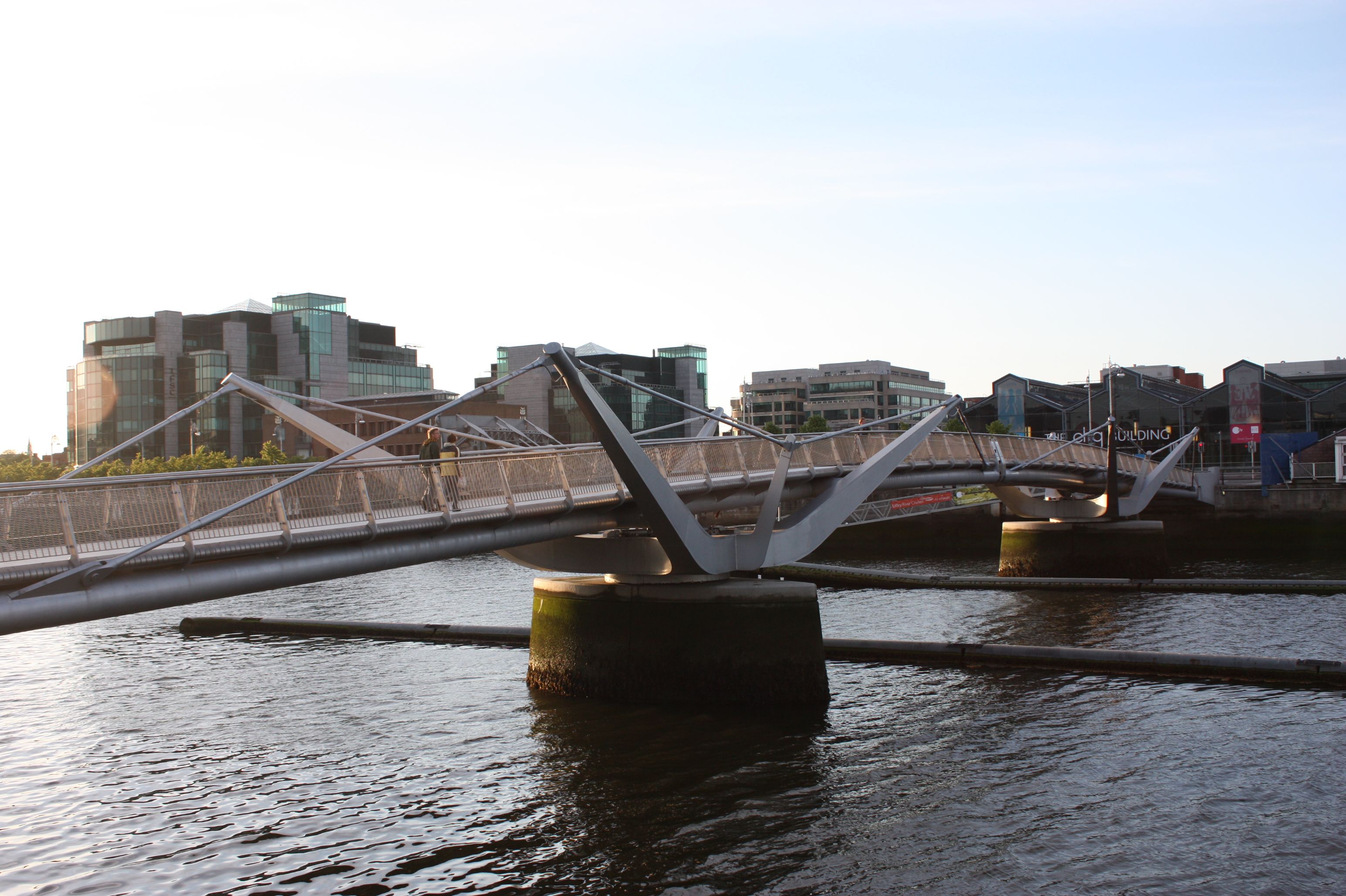 Pedestrian bridge spans the Liffey River in Dublin at sunset, highlighting modern architecture.