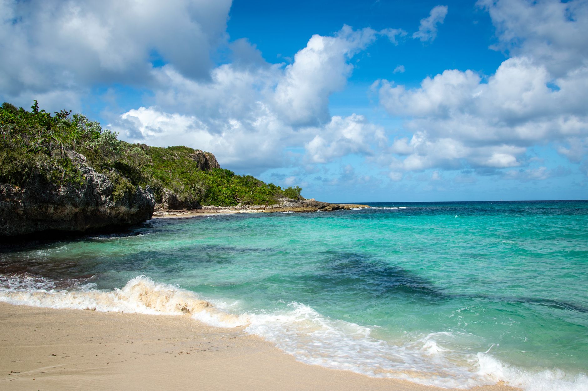 A picturesque beach with turquoise waters and rocky cliffs under a blue sky.