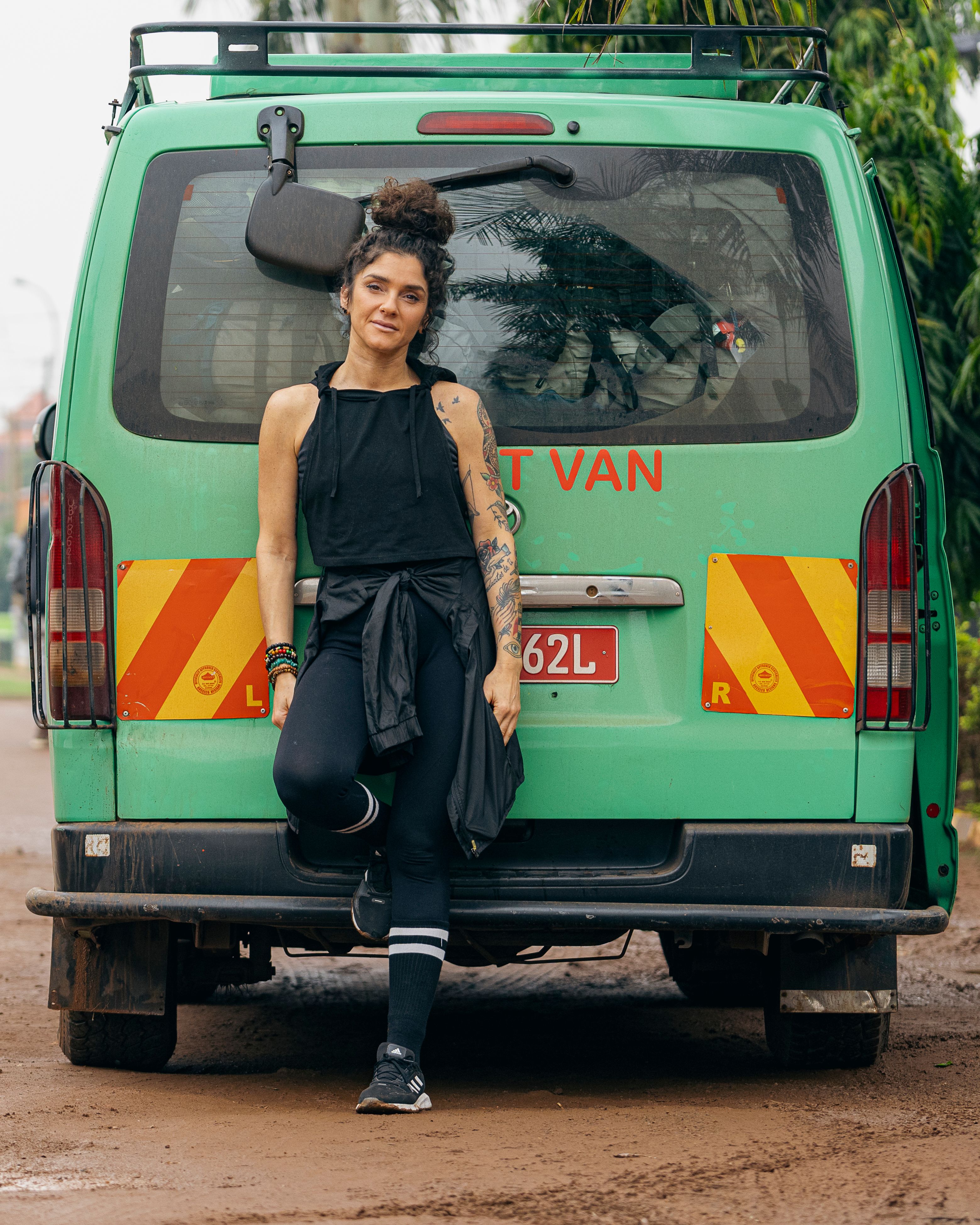 A fashionable woman poses confidently against a green van in an outdoor setting.