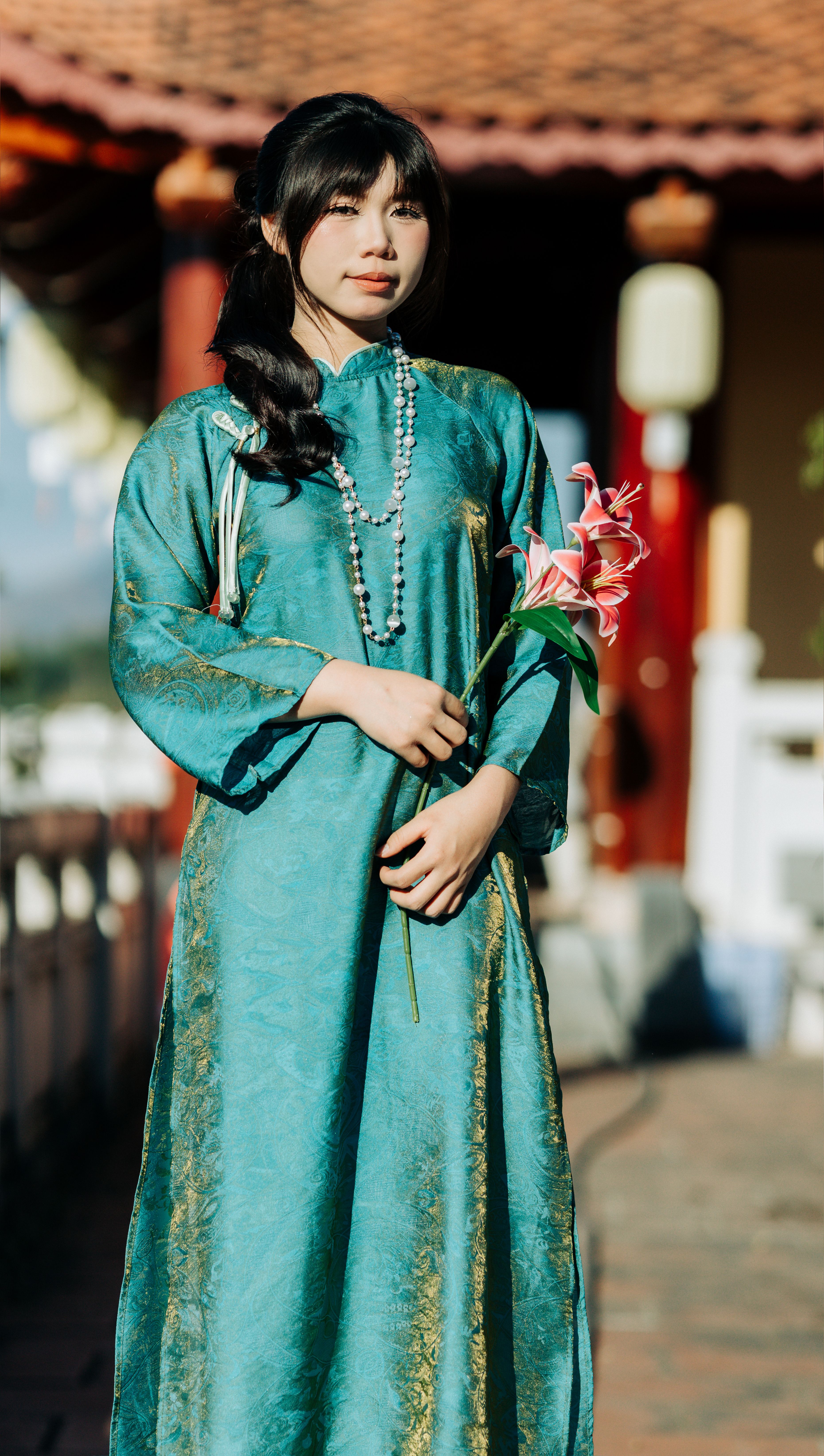 Young woman in traditional Vietnamese attire holding lilies at a temple in Kon Tum, Vietnam.