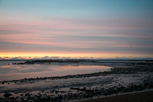 Free A serene seaside landscape at sunset, showcasing pink and blue skies reflected in tide pools. Stock Photo