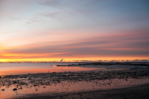 Free A captivating sunset over a rocky beach with colorful skies and calm waters. Stock Photo