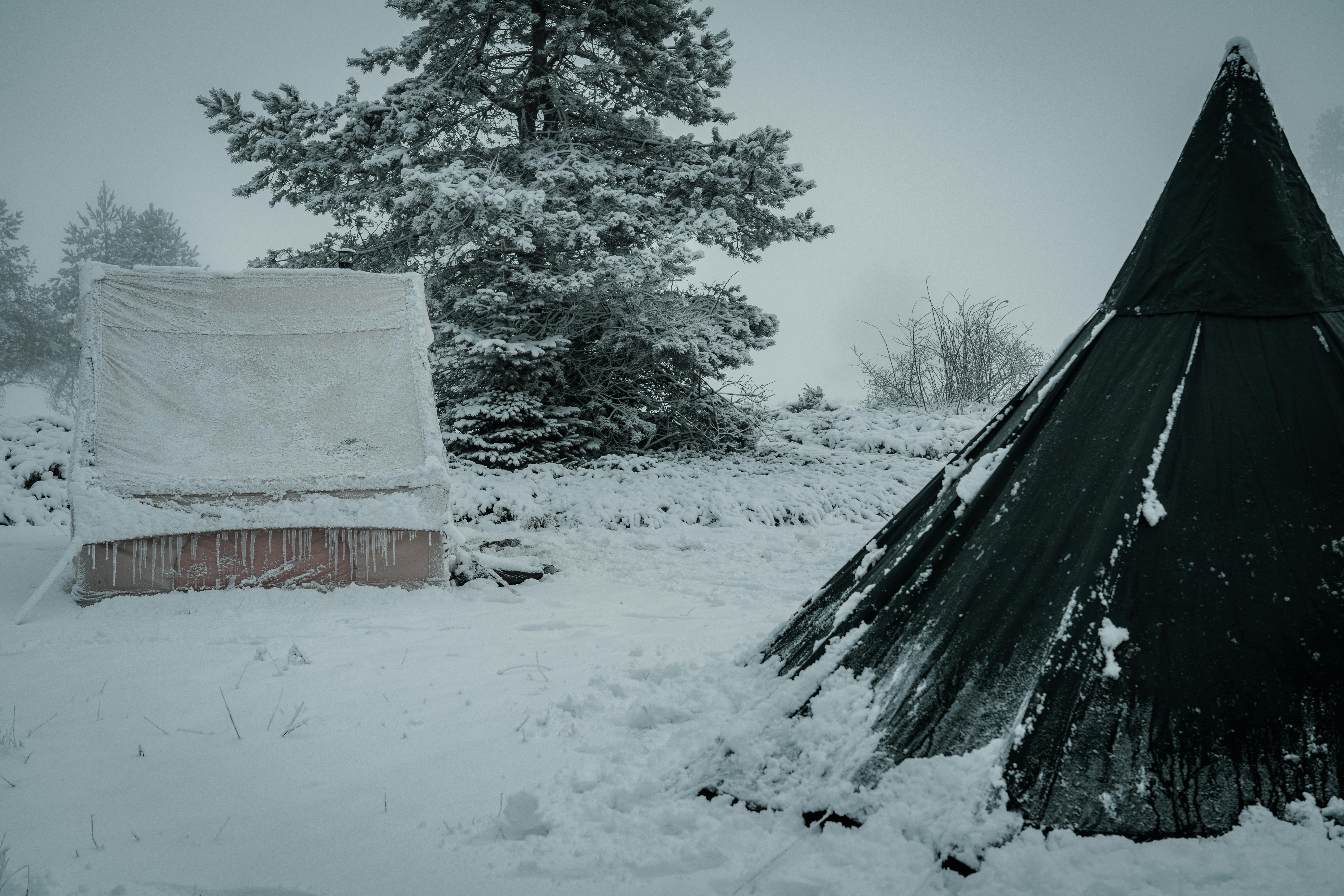 Des tentes enneigées dans un paysage hivernal, dépeignant une scène de camping en plein air sereine et glaciale.