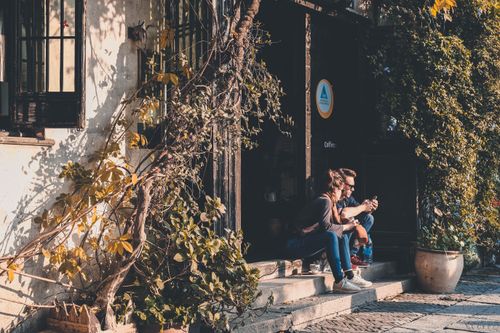 Free A couple enjoys a quiet moment on the steps of a charming, plant-adorned cafe. Stock Photo