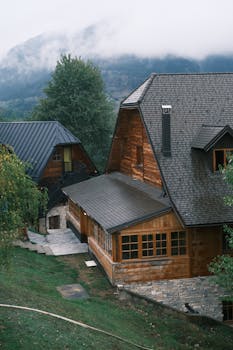 A rustic mountain cabin surrounded by lush greenery and misty mountains.