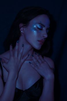 Artistic portrait of a woman with sparkling blue makeup in dim lighting, exuding elegance.