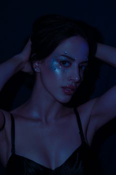 Mysterious woman in dark lighting with artistic blue makeup and highlights on her face.